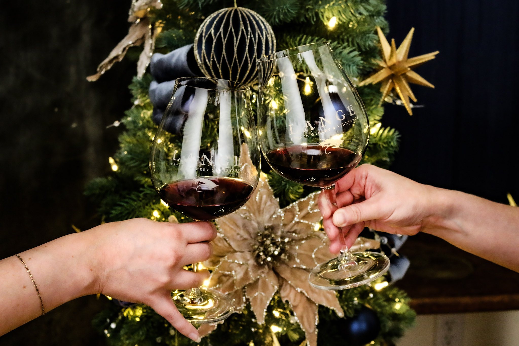 Two glasses with the Lange logo cheers in front of a festive blue and gold decorated Christmas tree