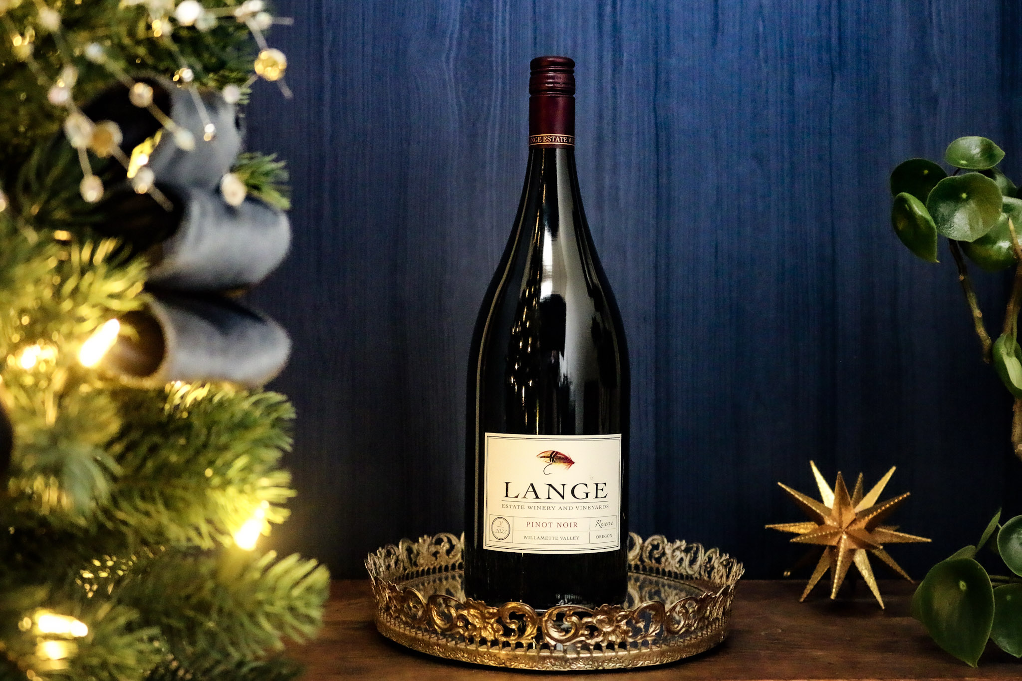 Magnum bottle of Pinot Noir Reserve in front of blue background next to Christmas tree